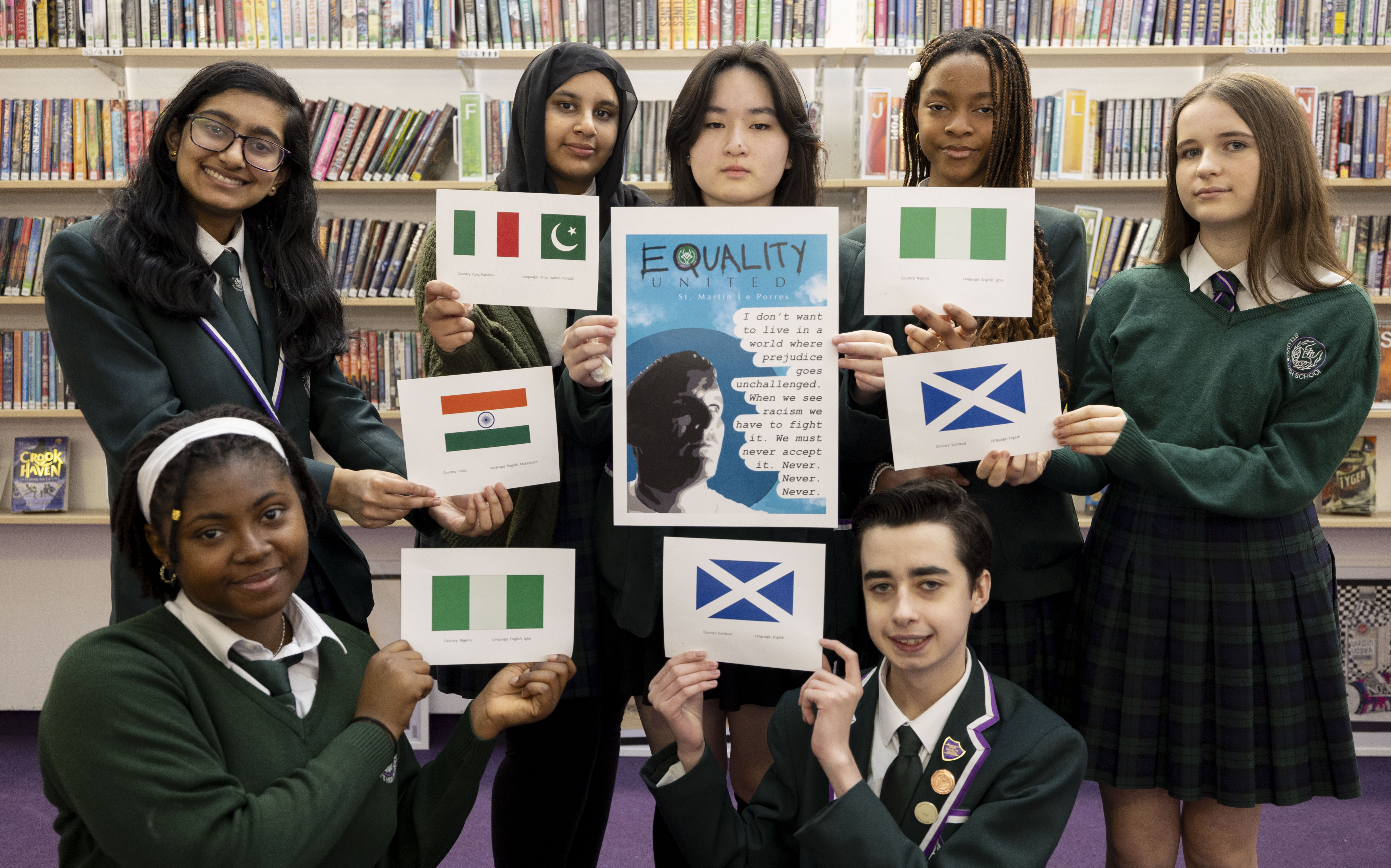 seven young people of different ethnicity wear green school uniforms  and smile. They each hold flags from different nations including Scotland, Nigeria and Pakistan . The person in the centre holds a sign reading "equality united, i don't want to live in a world where prejudice goes unchallenged. When we see racism, we have to fight it. We must never accept it. never. never. never"  
